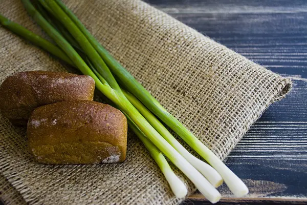 Freshly baked bread and green onion on a dark wooden background. — Stock Photo, Image