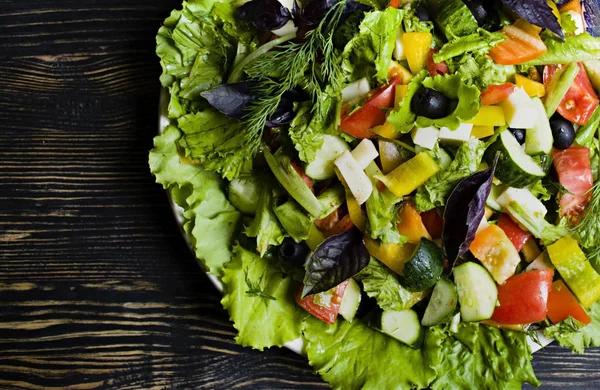 Ensalada griega con pepinos frescos, tomates, pimientos dulces, lechuga, cebolla roja, queso feta y aceitunas con aceite de oliva sobre un fondo de madera oscura . —  Fotos de Stock