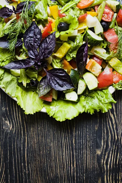 Salada grega com pepinos frescos, tomate, pimentão doce, alface, cebola vermelha, queijo feta e azeitonas com azeite sobre um fundo de madeira escura . — Fotografia de Stock