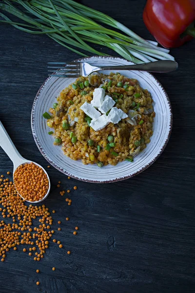 Lentil porridge with vegetables and herbs and fett cheese. Healthy lifestyle. Dietary menu. Dark wooden background. Side view.