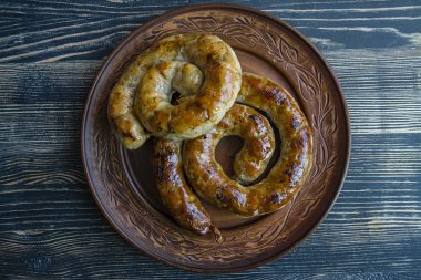Halka ev yapımı sosis pişirdim. Otlar ve baharatlar koyu ahşap arka plan üzerinde bir plaka ile kızarmış sosis. Yukarıdan görüntülemek.