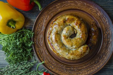 Kızarmış sosis otlar ve Baharatlar, ahşap arka plan ile. Ve ev yapımı sosis pişmiş halka. Yeşiller ve sebze ile bir tabakta servis. Yan görünüm.