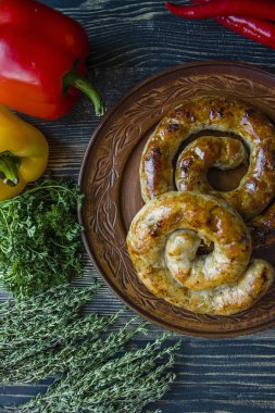 Kızarmış sosis otlar ve Baharatlar, ahşap arka plan ile. Ve ev yapımı sosis pişmiş halka. Yeşiller ve sebze ile bir tabakta servis. Yan görünüm.