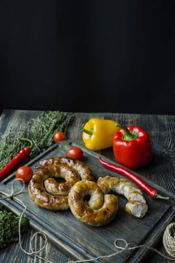 Kızarmış sosis otlar ve Baharatlar, ahşap arka plan ile. Ve ev yapımı sosis pişmiş halka. Bir ahşap tahta Yeşiller ve sebze ile servis. Yan görünüm.