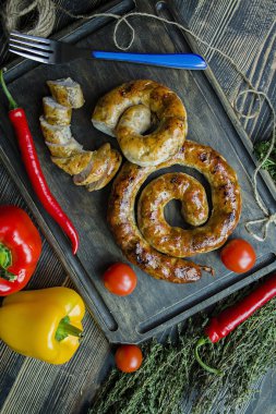 Kızarmış sosis otlar ve Baharatlar, ahşap arka plan ile. Ve ev yapımı sosis pişmiş halka. Ahşap bir gemide bir çatal, otlar ve sebze ile servis. Yukarıdan görüntülemek.