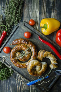 Kızarmış sosis otlar ve Baharatlar, ahşap arka plan ile. Ve ev yapımı sosis pişmiş halka. Ahşap bir gemide bir çatal, otlar ve sebze ile servis. Yukarıdan görüntülemek.