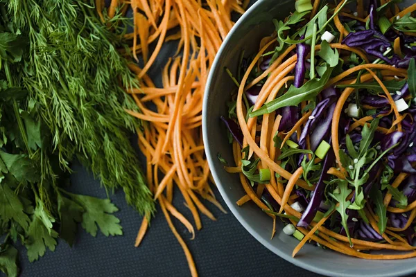 Салат из красной капусты, моркови и зелени. Украшен нарезанными овощами и травами. Резаные полоски. Темный фон . — стоковое фото