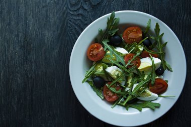 Taze domates, Arugula, yumurta, koyu ahşap arka planda zeytin yağı ile zeytin ile Yunan salatası. Sağlıklı yiyecekler. Veggie çanak.