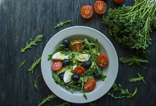 Греческий салат со свежими помидорами, рукколой, яйцами, оливками с оливковым маслом на темном фоне дерева. Здоровое питание. Овощное блюдо . — стоковое фото