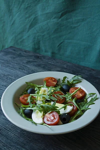 Görög saláta friss paradicsommal, arugula, tojás, olajbogyó, olívaolajjal, sötét fa háttérrel. Egészséges táplálkozás. Vega étel. — Stock Fotó