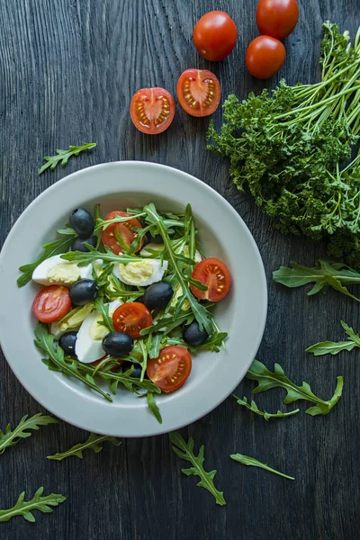 Görög saláta friss paradicsommal, arugula, tojás, olajbogyó, olívaolajjal, sötét fa háttérrel. Egészséges táplálkozás. Vega étel. — Stock Fotó