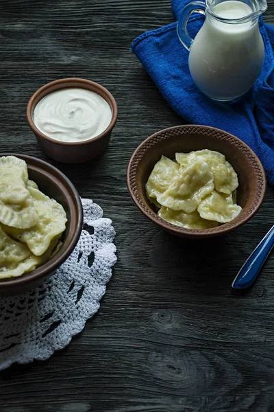 Dumplings med potatis och kål. Gräddfil, mjölk och gröna. Traditionell maträtt i Ukraina. Mörkt trä bakgrund. — Stockfoto