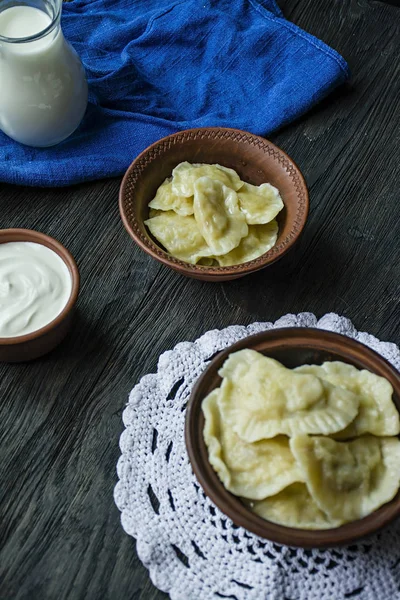 Dumplings med potatis och kål. Gräddfil, mjölk och gröna. Traditionell maträtt i Ukraina. Mörkt trä bakgrund. — Stockfoto
