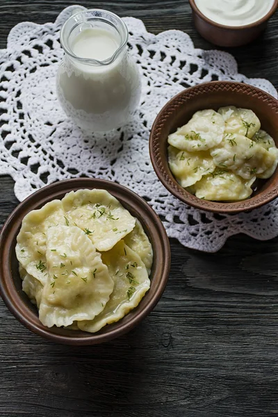 Dumplings con patatas y repollo. Crema agria, leche y verduras. Plato tradicional de Ucrania. Fondo de madera oscura . —  Fotos de Stock