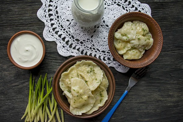 Dumplings med potatis och kål. Gräddfil, mjölk och gröna. Traditionell maträtt i Ukraina. Mörkt trä bakgrund. — Stockfoto