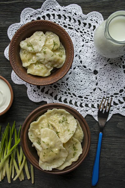 Dumplings med potatis och kål. Gräddfil, mjölk och gröna. Traditionell maträtt i Ukraina. Mörkt trä bakgrund. — Stockfoto