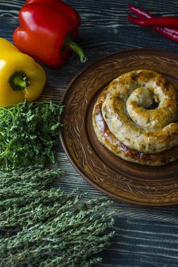 Kızarmış sosis otlar ve Baharatlar, ahşap arka plan ile. Ve ev yapımı sosis pişmiş halka. Yeşiller ve sebze ile bir tabakta servis. Yan görünüm.