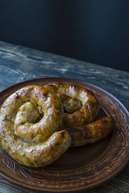Halka pişmiş ev yapımı sosis. Koyu ahşap bir arka plan üzerinde bir tabakta otlar ve baharatlar ile Kızarmış sosis. Yan görünüm.