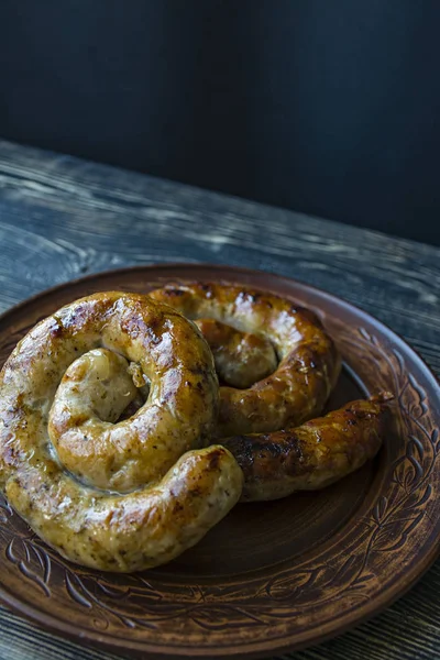 Halka pişmiş ev yapımı sosis. Koyu ahşap bir arka plan üzerinde bir tabakta otlar ve baharatlar ile Kızarmış sosis. Yan görünüm.