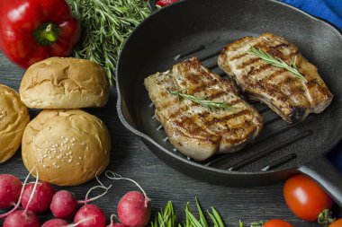 Siyah ahşap arka planda et, biberiye, yeşillikler ve sebzeler için baharatlar ile süslenmiş yuvarlak ızgara tavada ızgara biftek.