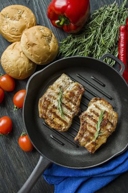 Siyah ahşap arka planda et, biberiye, yeşillikler ve sebzeler için baharatlar ile süslenmiş yuvarlak ızgara tavada ızgara biftek.