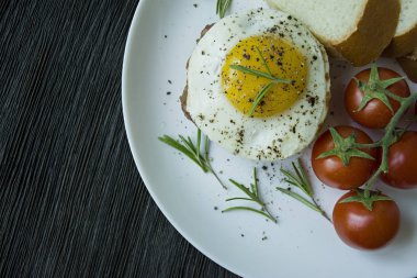 Baharatlarda kızarmış yumurtalı biftek. Biberiye, taze kiraz ve ekmek dilimleri ile dekore edilmiştir. Beyaz bir tabakta. Koyu ahşap arka plan. Yukarıdan görüntüle.
