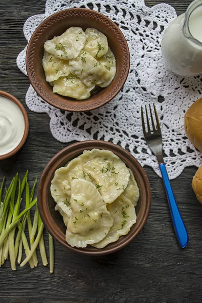 Dumplings med potatis och kål. Gräddfil, mjölk och gröna. Traditionell maträtt i Ukraina. Mörkt trä bakgrund. — Stockfoto