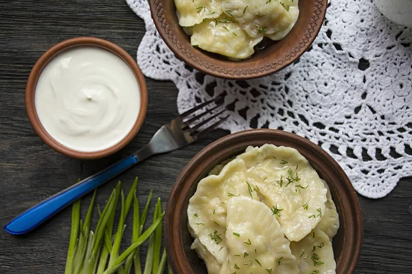 Dumplings con patatas y repollo. Crema agria, leche y verduras. Plato tradicional de Ucrania. Fondo de madera oscura . —  Fotos de Stock