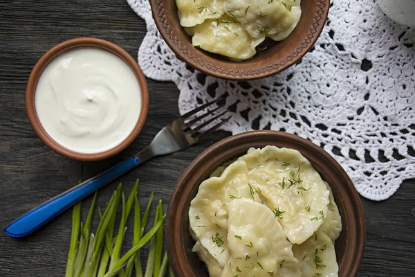 Dumplings avec pommes de terre et chou. Crème sure, lait et légumes verts. Plat traditionnel de l'Ukraine. Fond en bois foncé . — Photo