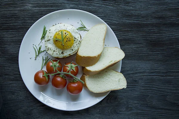 Marha steak tükörtojással fűszerekkel. Rozmaringos, friss Cseresznyés és kenyérszelet díszítve. Benyújtani egy fehér lemez. Sötét fából készült háttér. Oldalnézetből. Szóköz a szöveghez. — Stock Fotó