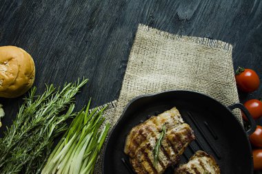 Yuvarlak bir ızgara tavada ızgara biftek, et, biberiye, yeşillik ve koyu ahşap arka plan üzerinde sebze için baharat ile süslenmiş. Metin için yer.