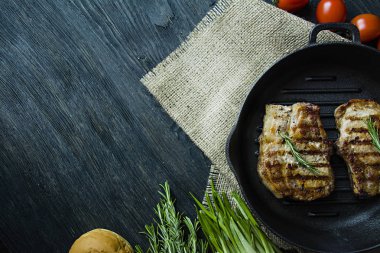 Yuvarlak bir ızgara tavada ızgara biftek, et, biberiye, yeşillik ve koyu ahşap arka plan üzerinde sebze için baharat ile süslenmiş. Metin için yer.