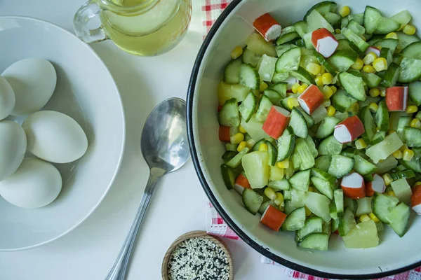 Ensalada con maíz, palitos de cangrejo, pepinos en un bol blanco sobre un fondo blanco. Ensalada vegetariana. Proceso de cocción . —  Fotos de Stock