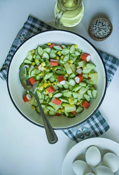 Salat mit Mais, Krabbenstangen, Gurken in einer weißen Schüssel auf weißem Hintergrund. vegetarischer Salat. Kochprozess. — Stockfoto