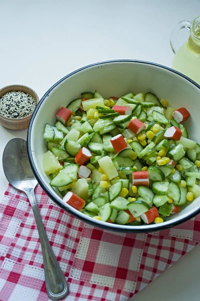 Salat mit Mais, Krabbenstangen, Gurken in einer weißen Schüssel auf weißem Hintergrund. vegetarischer Salat. Kochprozess. — Stockfoto