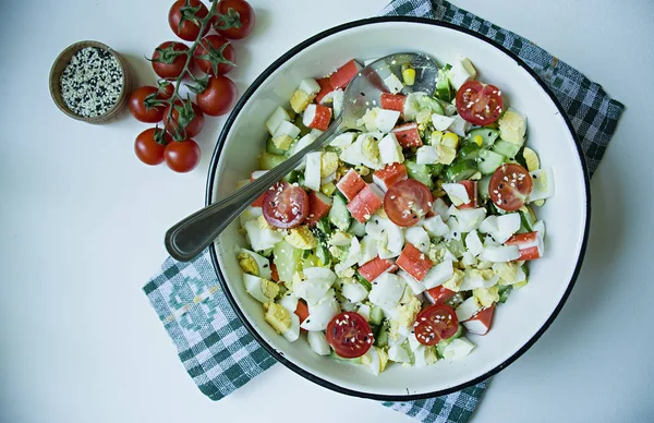 Salat mit Mais, Krabbenstangen, Gurken in einer weißen Schüssel auf weißem Hintergrund. vegetarischer Salat. Kochprozess. — Stockfoto