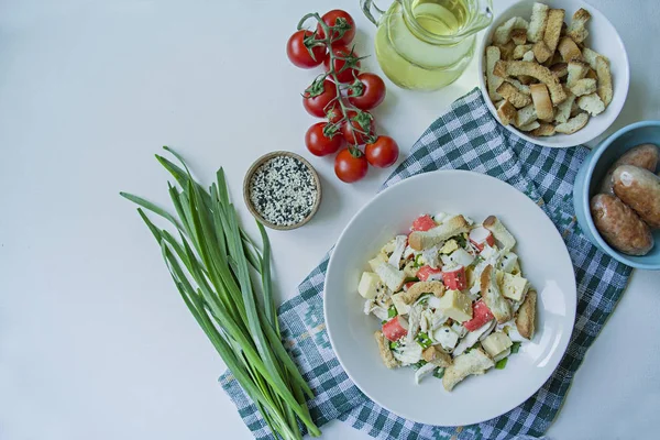 Salat mit Crackern, Krabbenstangen, Hühnerfilet, frischen Kräutern und Hartkäse, gewürzt mit Olivenöl, serviert auf einem weißen Teller. Blick von oben. weißer Hintergrund. — Stockfoto