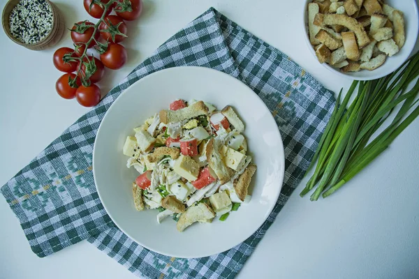 Ensalada con galletas saladas, palitos de cangrejo, filete de pollo, hierbas frescas y queso duro sazonado con aceite de oliva servido en un plato blanco. Vista desde arriba. Fondo blanco . —  Fotos de Stock