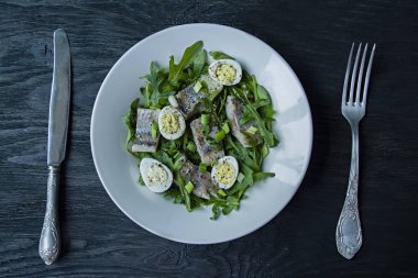 Arugula, soğan, haşlanmış bıldırcın yumurtası ve limon suyu ve zeytinyağı ile marinated ringa balığı. Lezzetli salata. Doğru beslenme. Koyu ahşap arka plan.