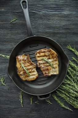 Siyah ahşap arka planda et, biberiye, yeşillikler ve sebzeler için baharatlar ile süslenmiş yuvarlak ızgara tavada ızgara biftek.