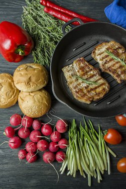 Siyah ahşap arka planda et, biberiye, yeşillikler ve sebzeler için baharatlar ile süslenmiş yuvarlak ızgara tavada ızgara biftek.