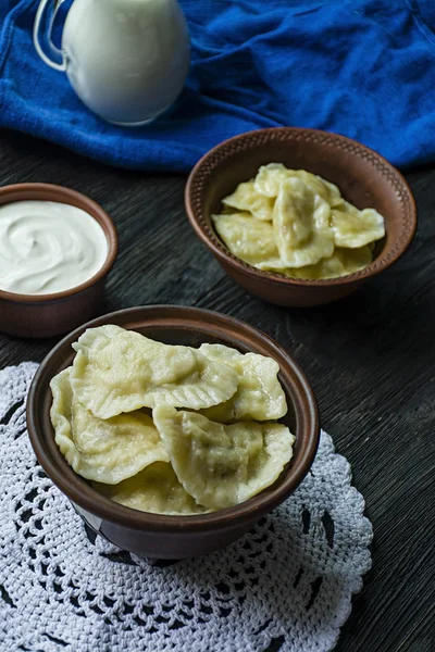 Dumplings met aardappelen en kool. Zure room, de melk en de Groenen. Traditionele schotel van Oekraïne. Donkere houten achtergrond. — Stockfoto