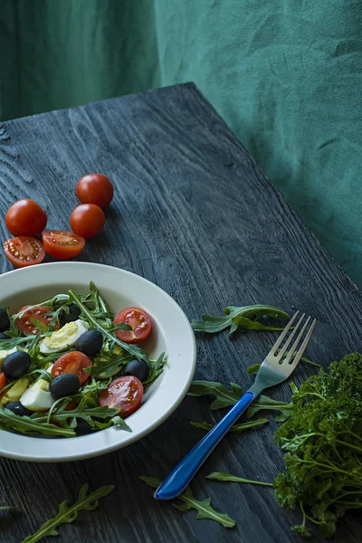 Ensalada griega con tomates frescos, rúcula, huevos, aceitunas con aceite de oliva sobre un fondo de madera oscura. Comida saludable. Plato de verduras . —  Fotos de Stock