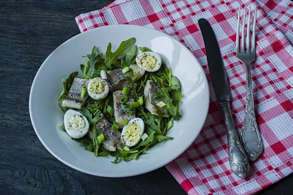 Marinierter Hering mit Rucola, Zwiebeln, gekochten Wachteleiern und Zitronensaft und Olivenöl. leckerer Salat. Richtige Ernährung. dunkler Holzhintergrund. — Stockfoto