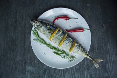 Beyaz bir tabakta limonlu uskumru. Taze biberiye, biber biberiye ile dekore edilmiştir. Uskumru ızgarası. Yukarıdan görüntüleyin. Koyu ahşap arka plan.