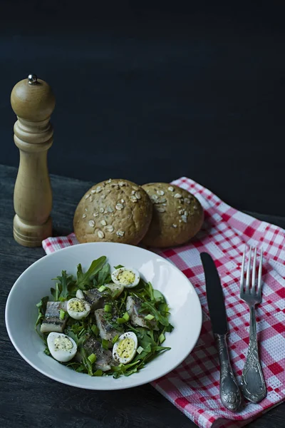 Hareng mariné avec roquette, oignons, oeufs de caille bouillis et jus de citron et huile d'olive. Délicieuse salade. Une bonne nutrition. Fond en bois foncé . — Photo