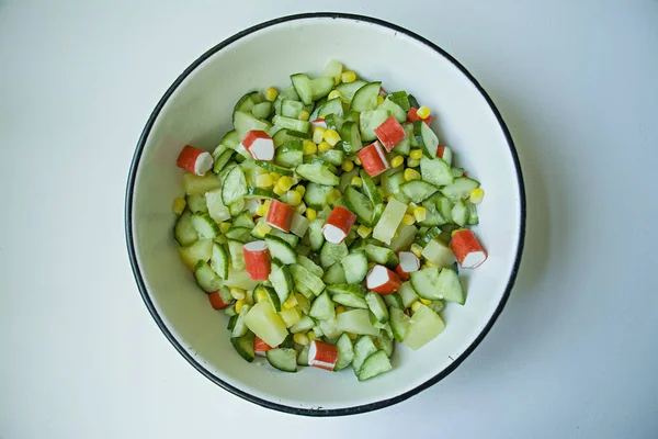 Salat mit Mais, Krabbenstangen, Gurken in einer weißen Schüssel auf weißem Hintergrund. vegetarischer Salat. Kochprozess. — Stockfoto