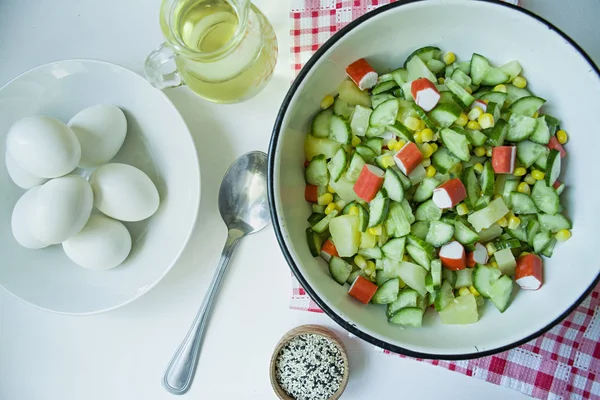 Salat mit Mais, Krabbenstangen, Gurken in einer weißen Schüssel auf weißem Hintergrund. vegetarischer Salat. Kochprozess. — Stockfoto