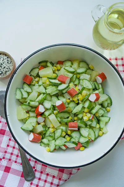 Salat mit Mais, Krabbenstangen, Gurken in einer weißen Schüssel auf weißem Hintergrund. vegetarischer Salat. Kochprozess. — Stockfoto