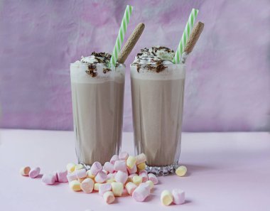 Dondurma ve krem şanti, marshmallow, kurabiye, waffle ile çikolatalı milkshake, bir cam bardak servis. Açık arka plan.